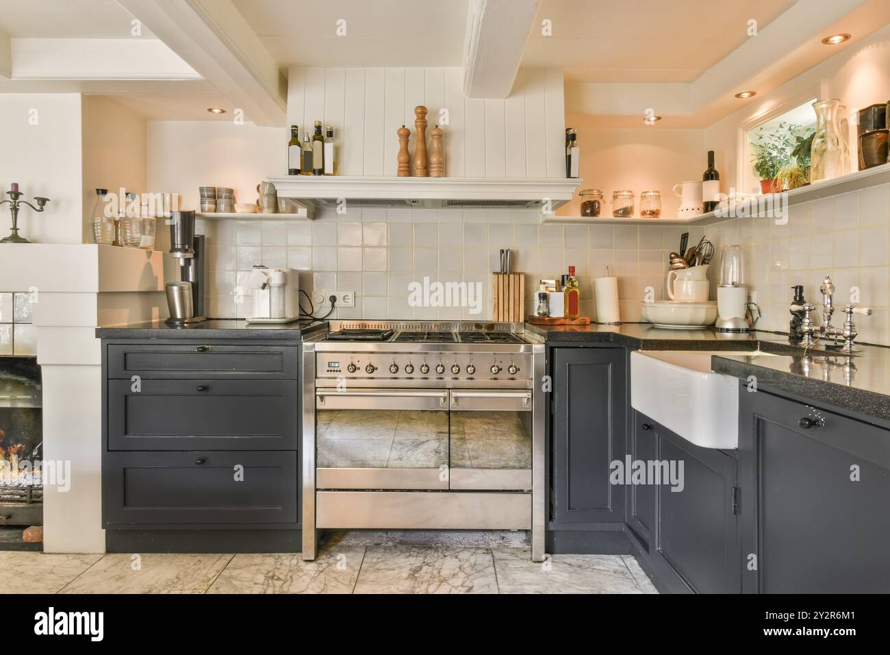 Eleganti e moderni interni della cucina con mobili neri, fornello in acciaio inox e ripiani in granito con luce naturale. Foto Stock