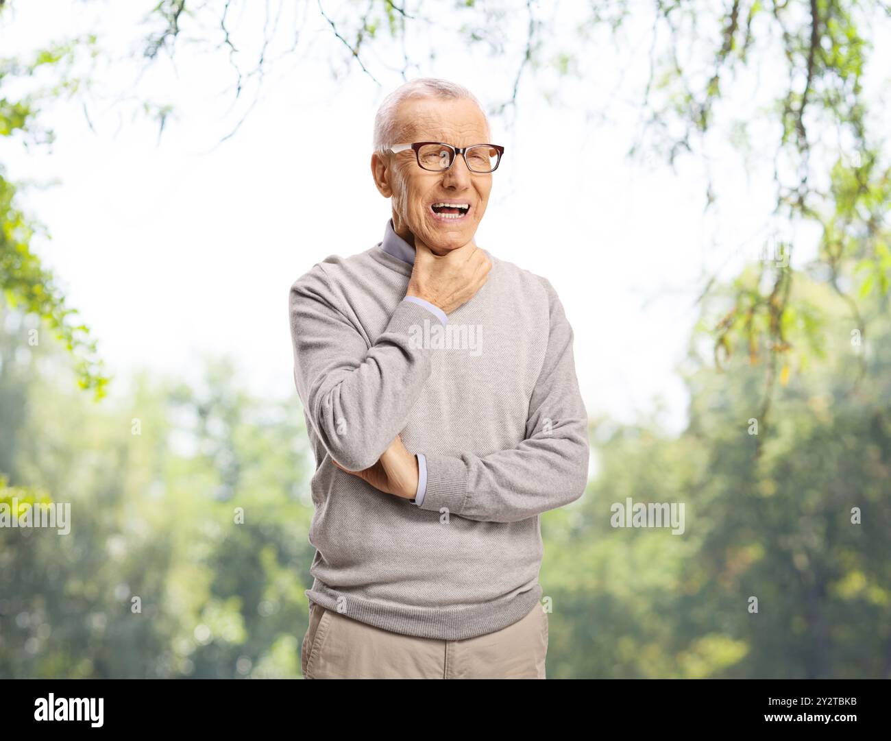 Uomo anziano con mal di gola in piedi all'aperto in un parco Foto Stock