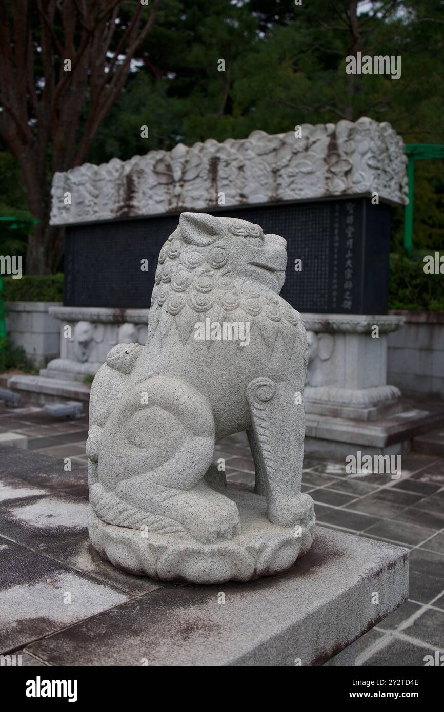Statua in pietra di un leone guardiano in un tempio con alberi sullo sfondo. Foto Stock