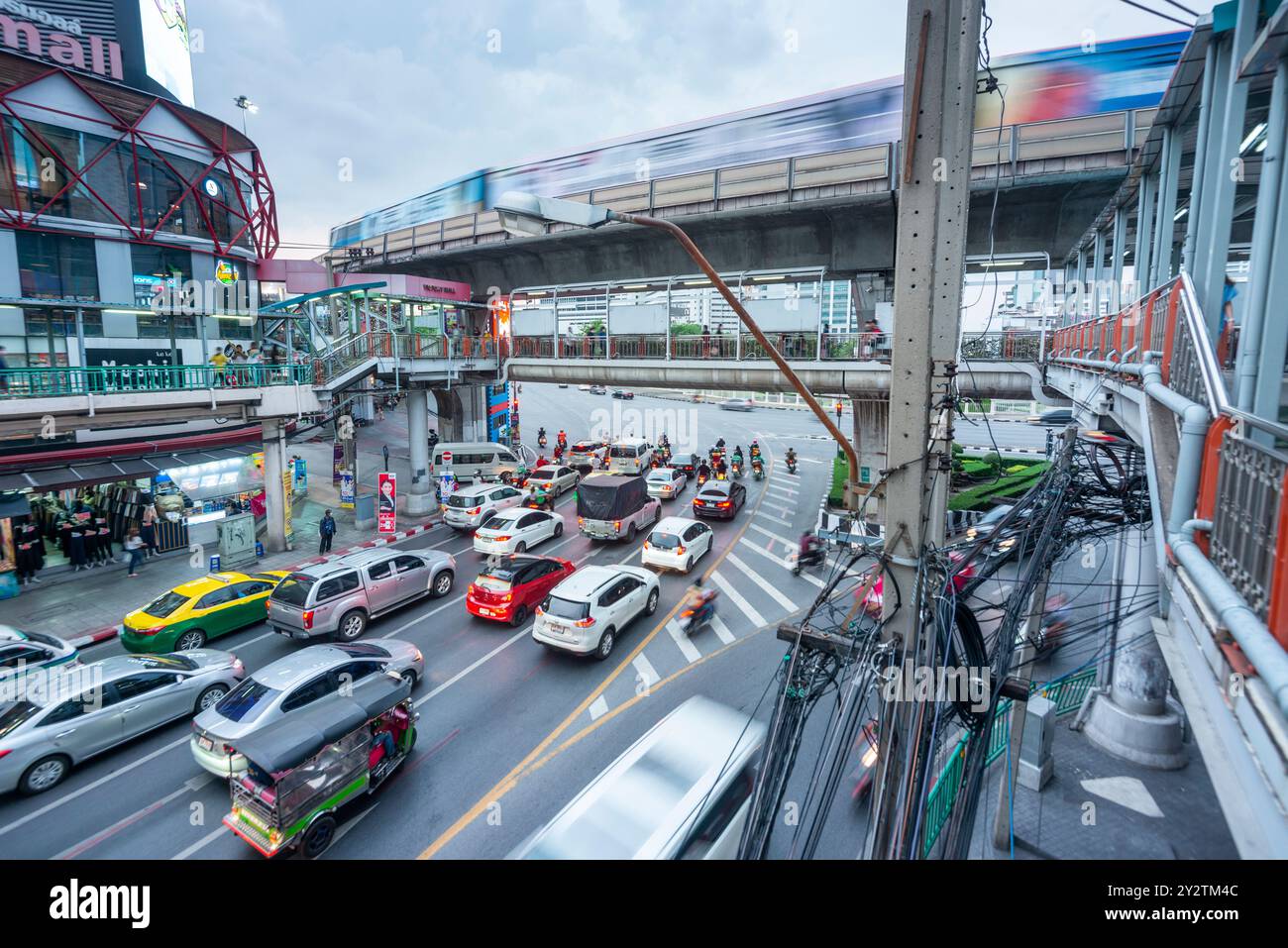 Infinite linee di veicoli, striature di movimento sfocate, corsa verso e fuori, sotto un passaggio pedonale, e linea ferroviaria sopraelevata in cemento sopraelevato Skytrain, passante Foto Stock