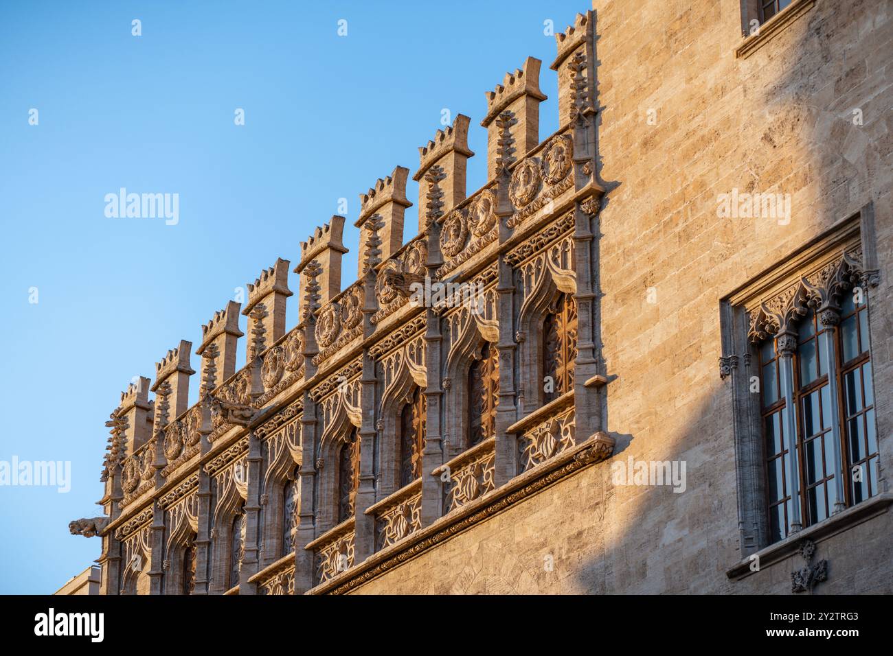 Le intricate pareti in pietra e le finestre splendidamente lavorate di un'impressionante facciata di struttura storica che si crogiola alla luce calda del sole a Valencia, Spagna Foto Stock