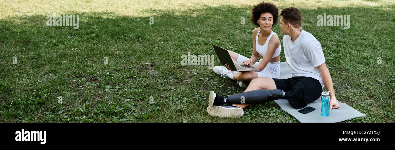 Due amici che usano un notebook sull'erba, dimostrando forza, resilienza e amicizia. Foto Stock
