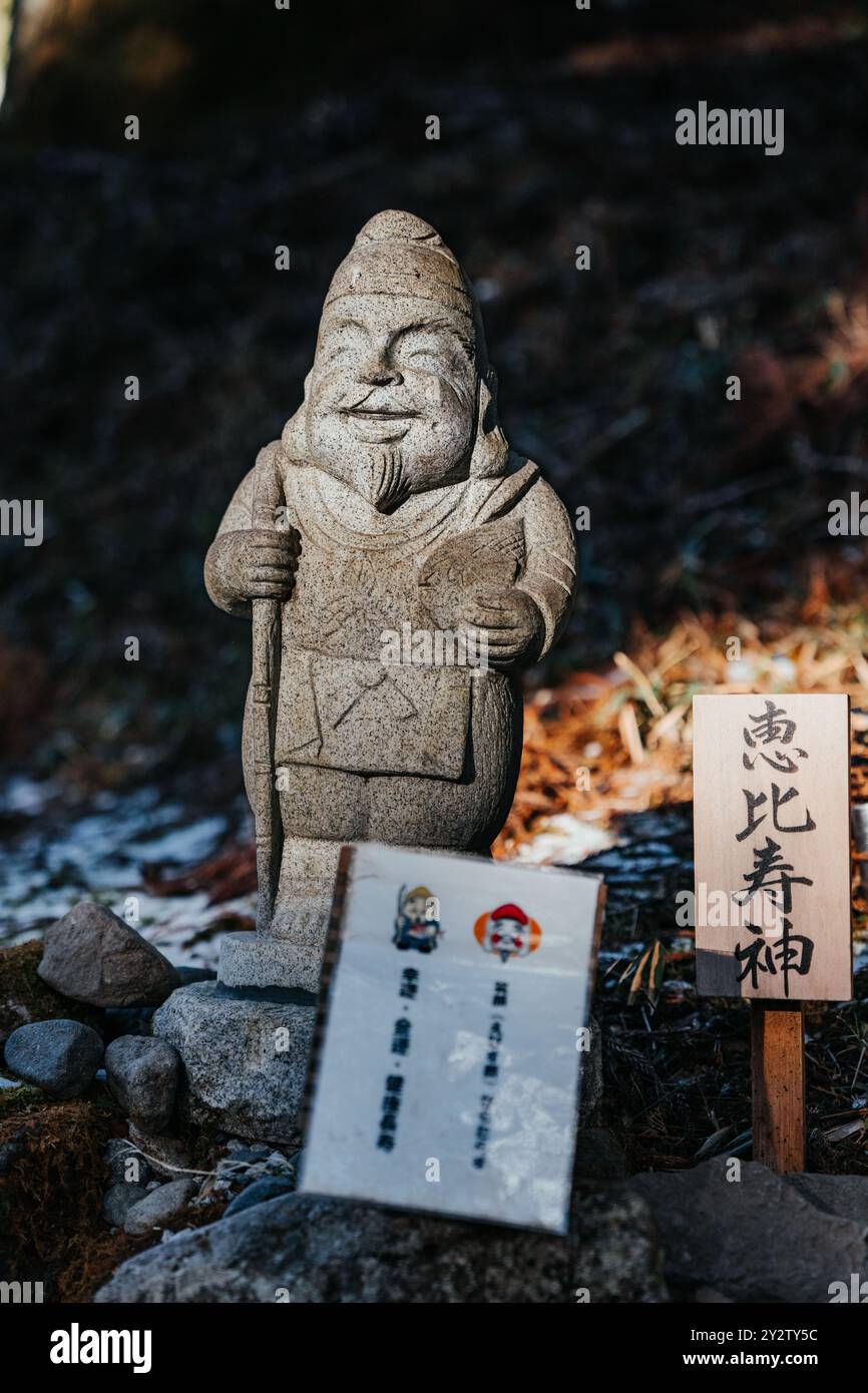 Statua di pietra di una figura sorridente con segni giapponesi in un ambiente naturale all'aperto Foto Stock