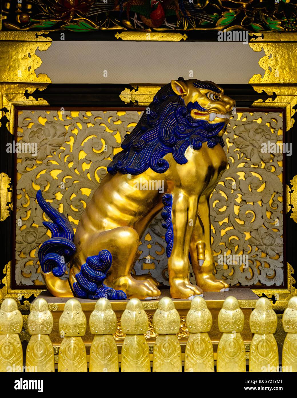 Un dettagliato primo piano di una statua di un leone dorato con accenti blu in un tempio giapponese, circondato da intricati intagli e decorazioni d'oro. Foto Stock