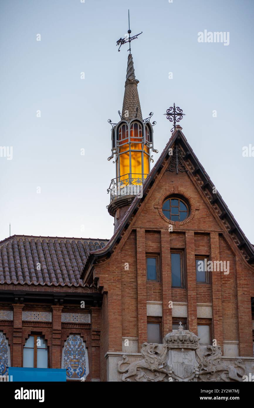 La guglia illuminata incorona graziosamente uno splendido edificio storico in mattoni, creando una pittoresca scena al crepuscolo di Valencia, Spagna Foto Stock