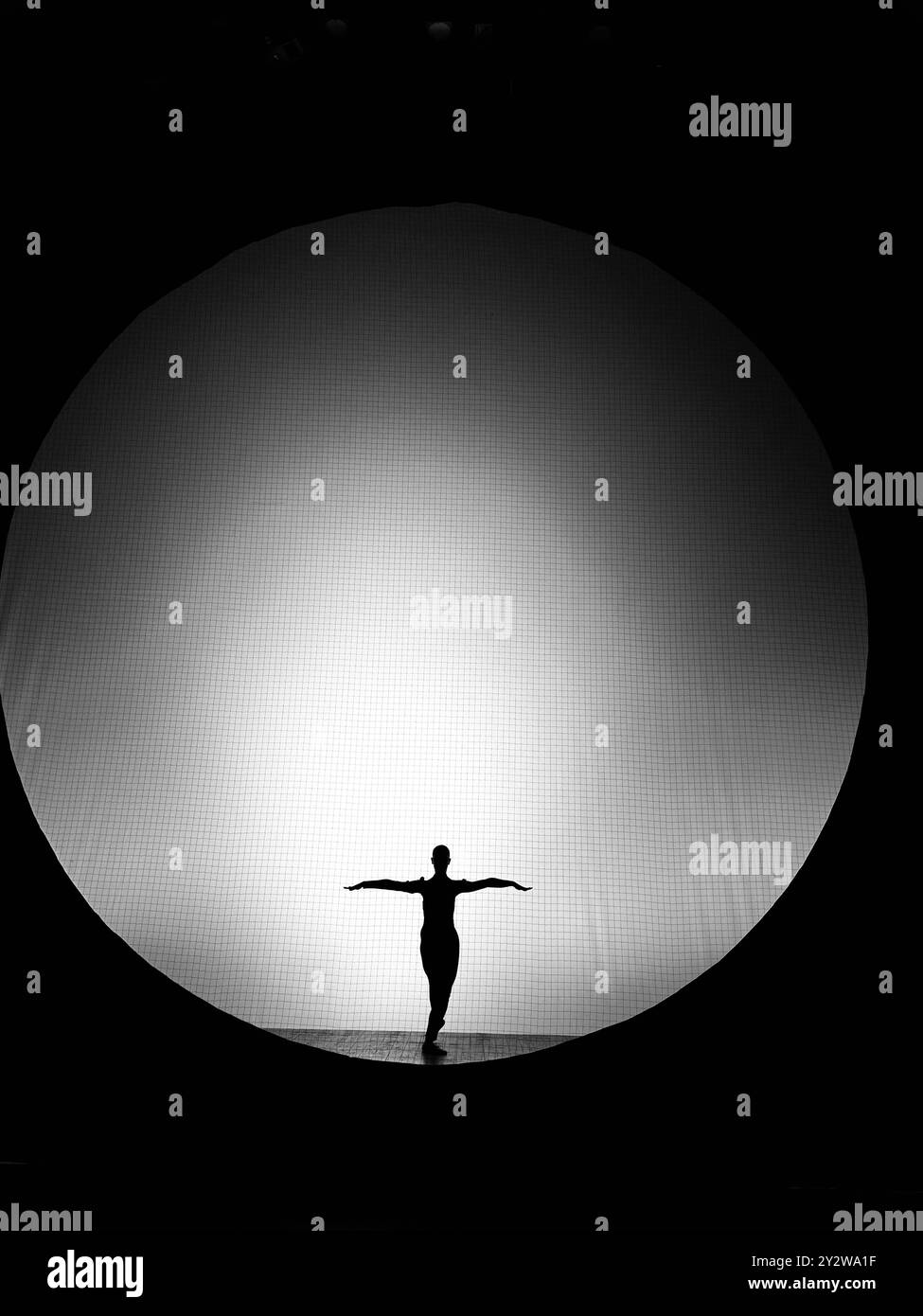 Silhouette di una ballerina con le braccia allungate davanti a un grande sfondo di luce circolare. Foto Stock