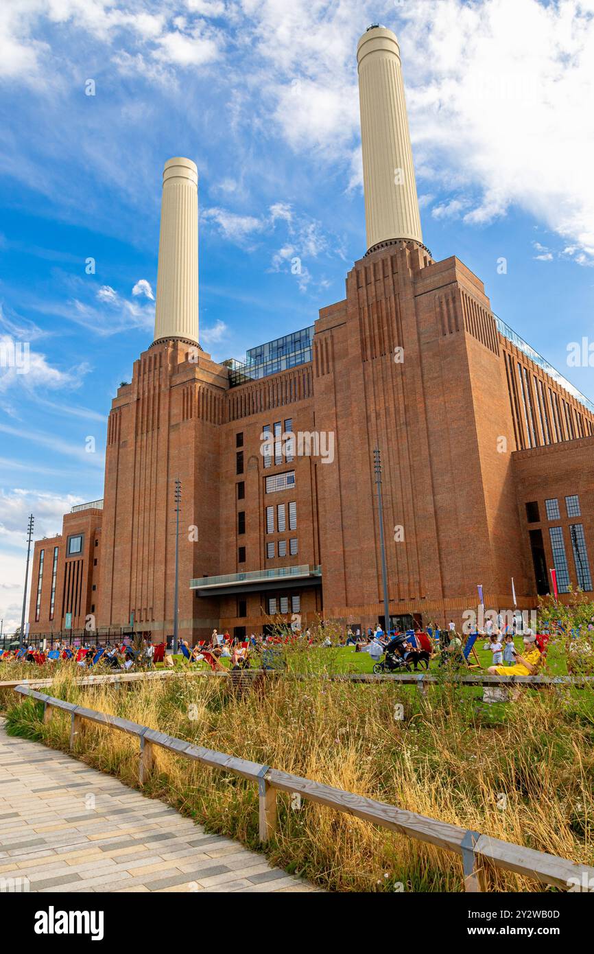 Persone sedute su sedie a sdraio sul prato di fronte alla centrale elettrica di Battersea, ora una delle principali destinazioni per il tempo libero e il commercio al dettaglio, Nine Elms, Londra Foto Stock