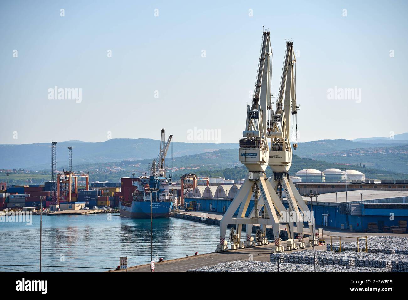 Capodistria, Slovenia - 25 agosto 2024: Porto di Capodistria con grandi gru portuali e navi portacontainer. Il porto simboleggia il traffico merci internazionale e l'importanza delle importazioni e delle esportazioni nella logistica globale *** Hafen von Koper mit großen Hafenkränen und Containerschiffen. Der Hafen symbolisiert den internationalen Güterverkehr und die Bedeutung von Import und Export in der globalen Logistik Foto Stock