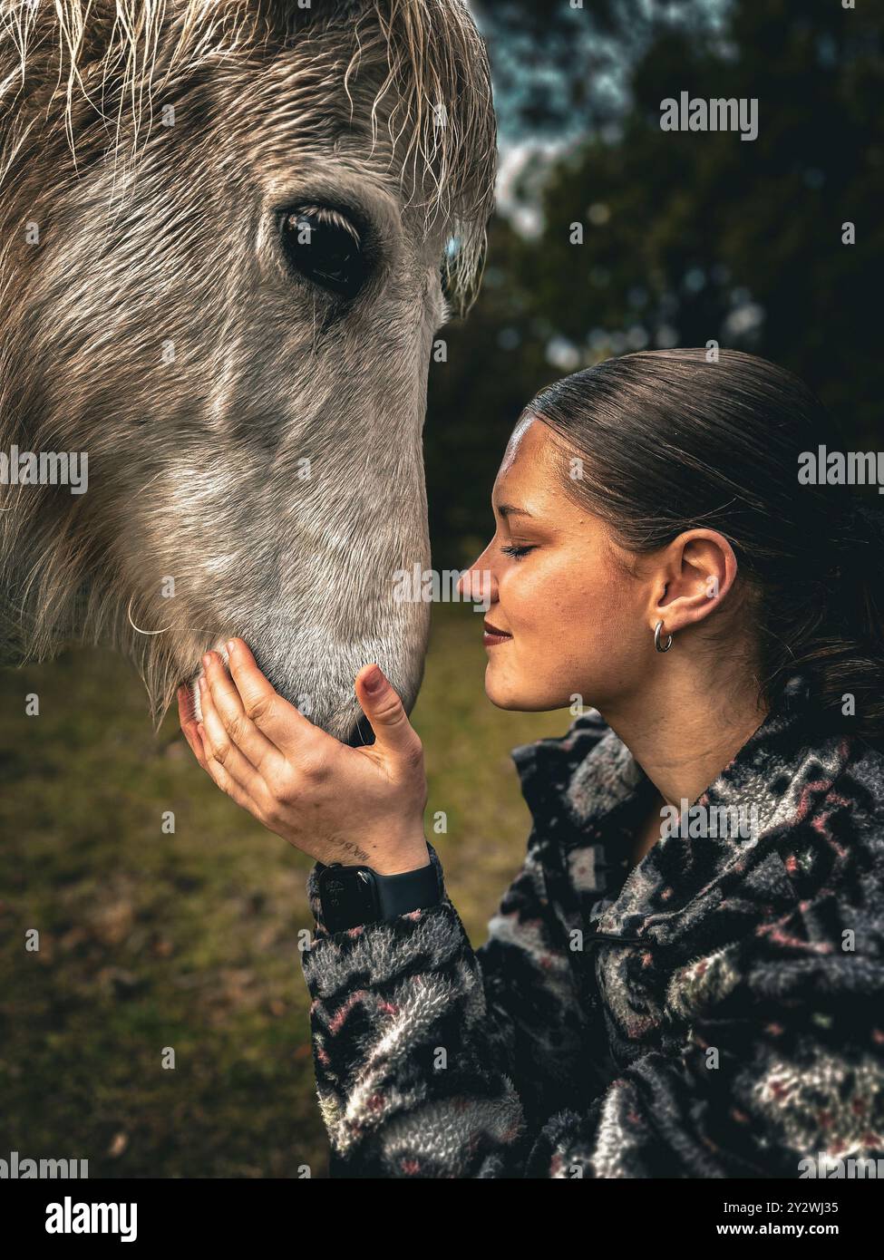 Una giovane donna che tocca dolcemente il volto di un cavallo, mostrando un profondo legame tra uomo e animale in un ambiente all'aperto. Foto Stock