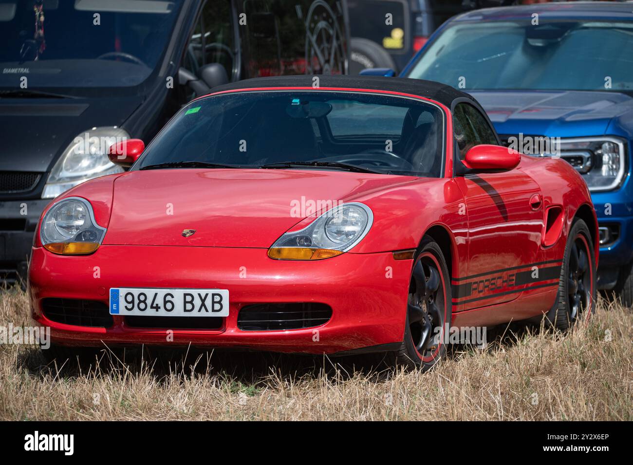 Porsche Boxster rossa 1996 di prima generazione parcheggiata in un parcheggio erboso. Si tratta di un'auto sportiva tedesca a due posti con cabriolet sul tetto in tela. Foto Stock