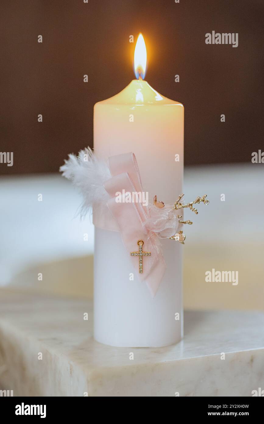 Un primo piano verticale di una candela battesimale con elementi decorativi su sfondo sfocato Foto Stock