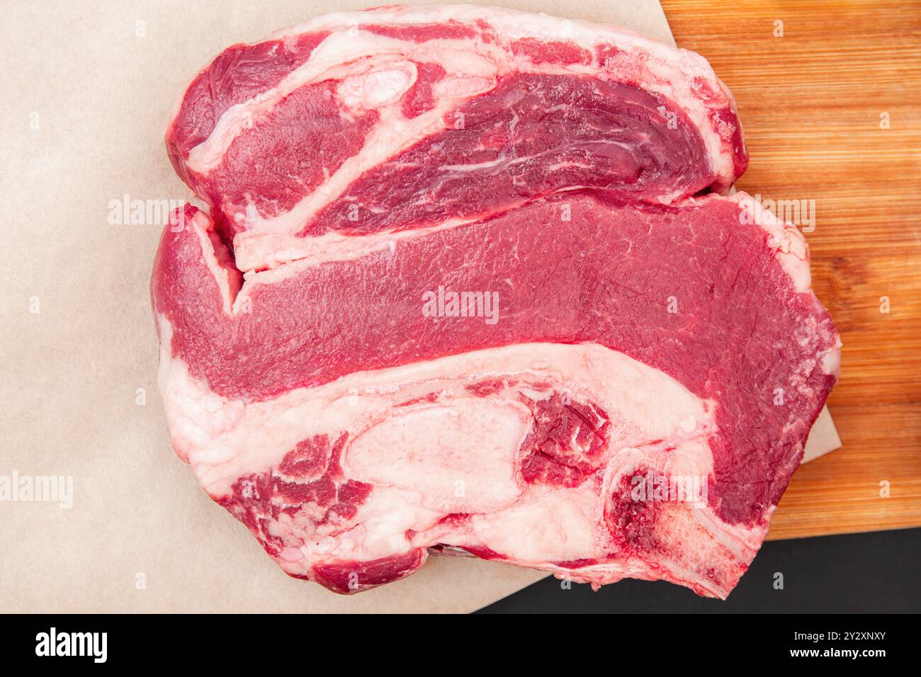 Bistecca di manzo crudo spessa su tagliere di legno con erbe aromatiche, bistecca pronta per essere condita e cotta Foto Stock