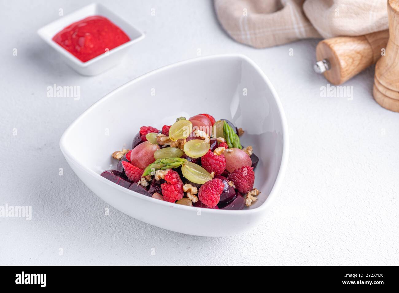 Un'insalata di frutta fresca e colorata con lamponi, uva e noci in una ciotola bianca con salsa rossa sul lato. Foto Stock