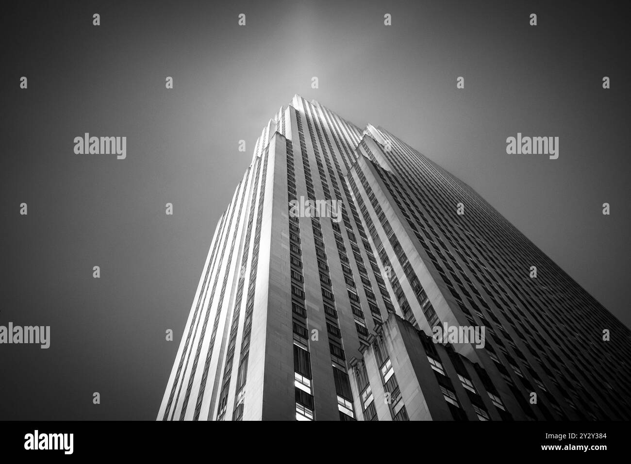 Foto in bianco e nero di un alto grattacielo con una prospettiva verso l'alto, che mostra i suoi dettagli architettonici contro un cielo limpido. Foto Stock