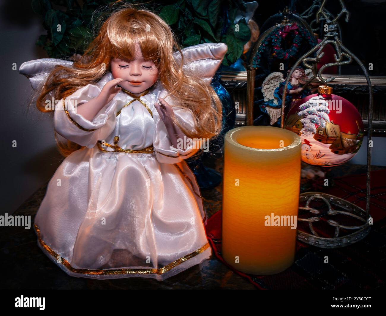 Bambola d'angelo vintage con ali bianche accanto a una candela luminosa e ornamento natalizio. Foto Stock