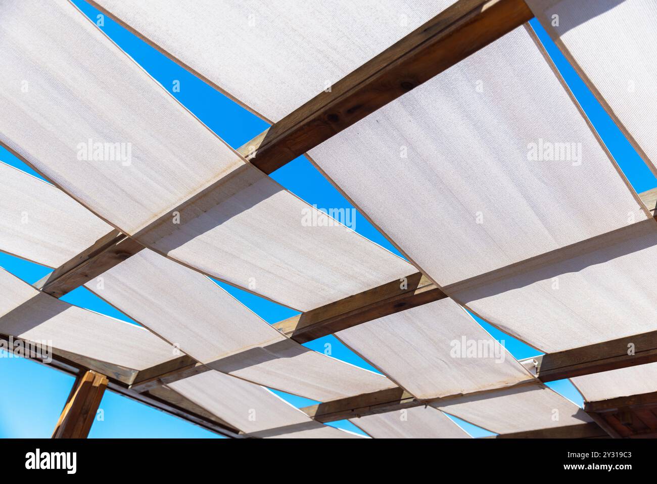 Il tetto della terrazza è realizzato con strisce di tessuto bianco su una struttura in legno e si trova sotto il cielo blu Foto Stock