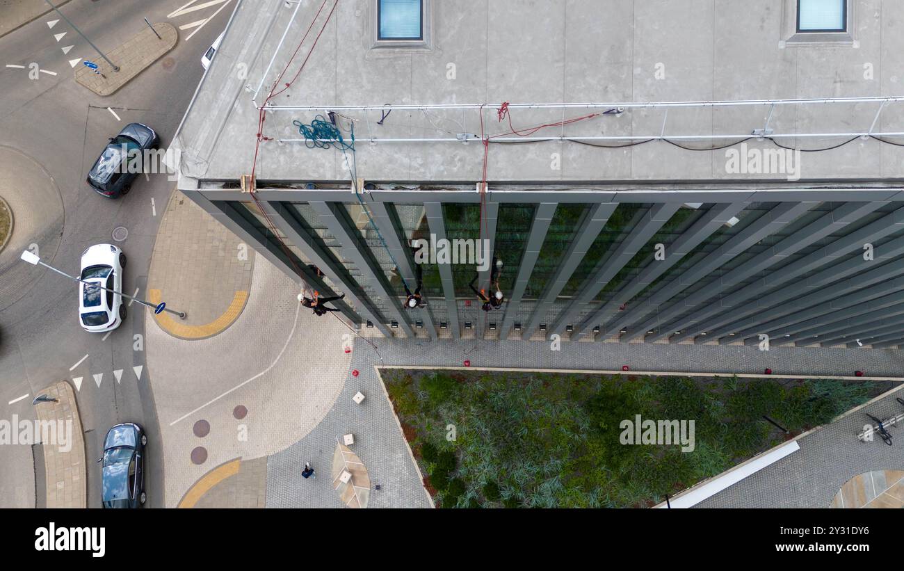 Operai che puliscono le finestre di un moderno edificio in vetro, sospeso su corda. Presenta una struttura alta con superfici riflettenti Foto Stock