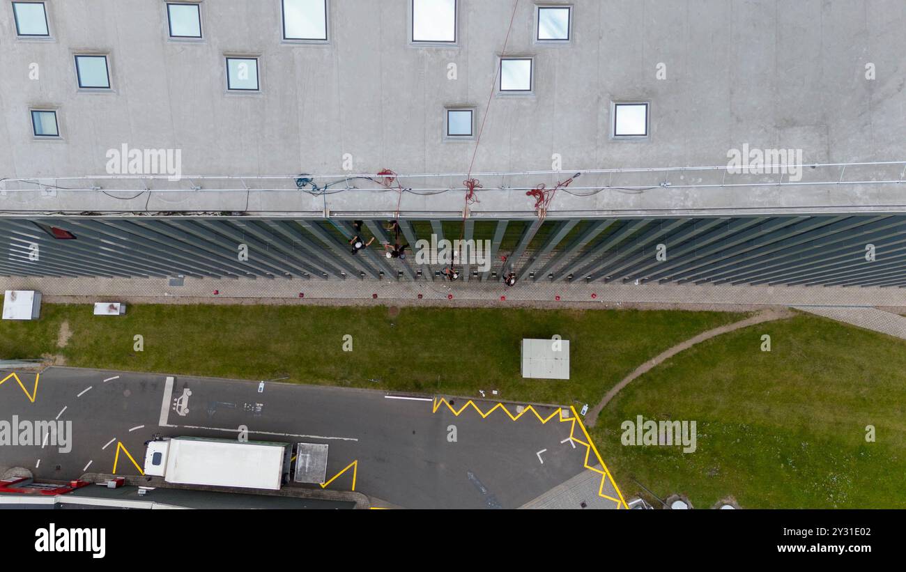 Operai che puliscono le finestre di un moderno edificio in vetro, sospeso su corda. Presenta una struttura alta con superfici riflettenti Foto Stock
