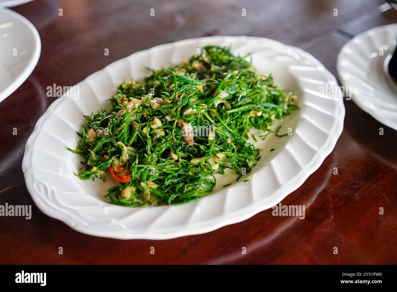 Le foglie di chakram fritte in olio assomigliano a foglie verdi. L'aglio viene fritto in padella con. Foto Stock