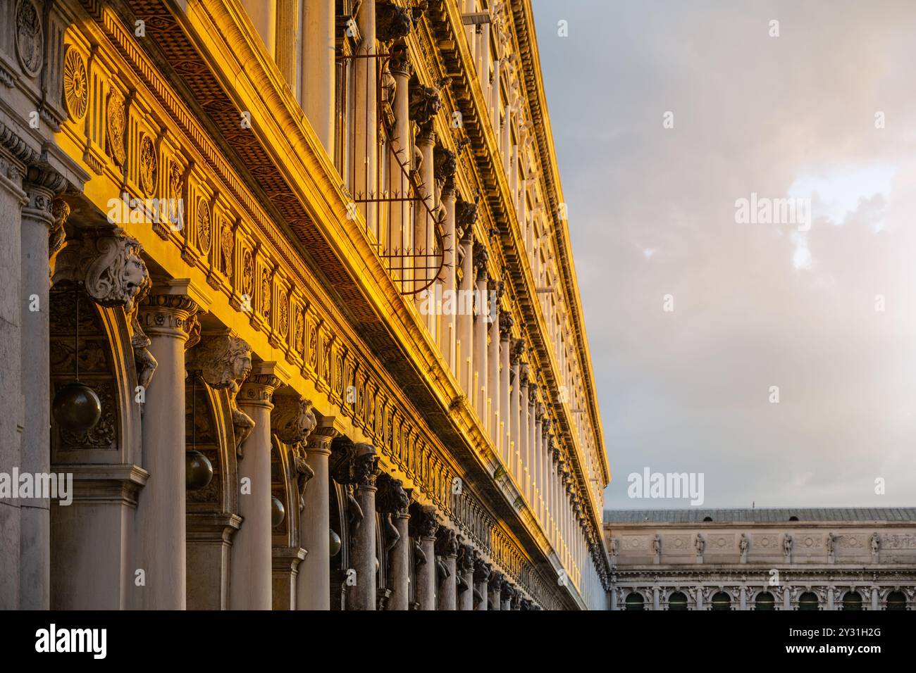 Le intricate caratteristiche architettoniche della nuova Procuracie di Venezia sono evidenziate dal caldo bagliore del sole che tramonta, che mostra colonne e disegni ornati contro un cielo spettacolare. Foto Stock