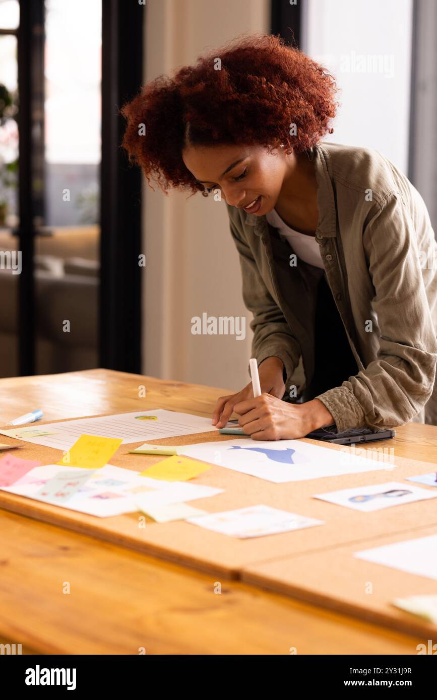 In ufficio, scrivendo su carta, donna che brava idee con note adesive colorate sul tavolo Foto Stock