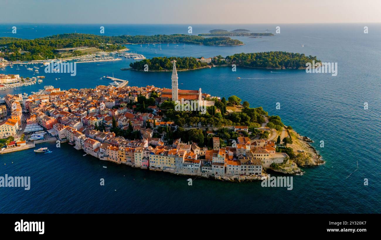 La luce del sole dorata bagna la città costiera di Rovigno, in Croazia, evidenziando la sua architettura storica e il vivace porto. Le barche saltano dolcemente in acqua mentre il giorno passa in una tranquilla serata. Foto Stock