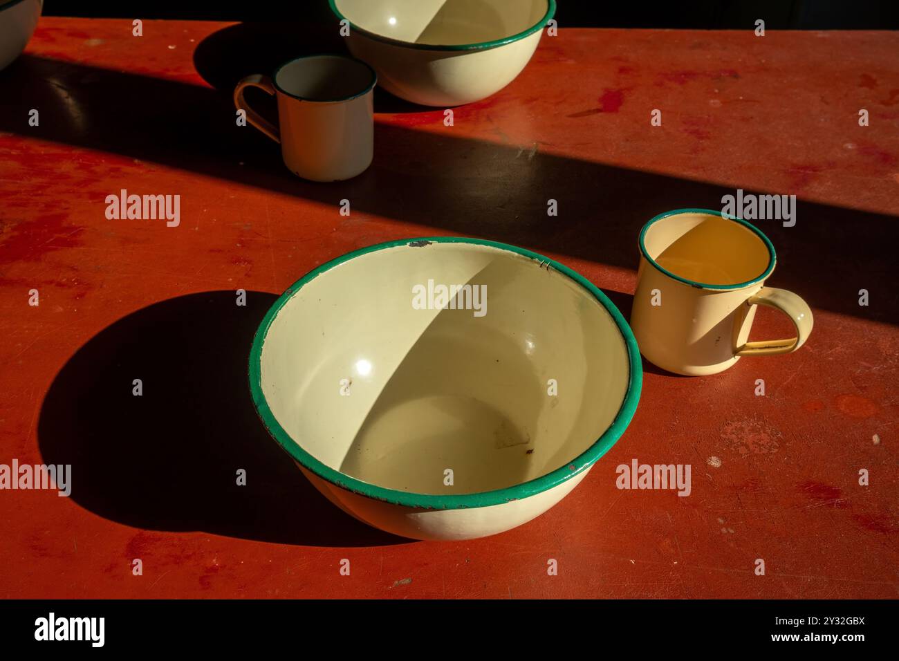 vecchie tazze e ciotole smaltate sul tavolo sotto la luce del sole all'interno Foto Stock