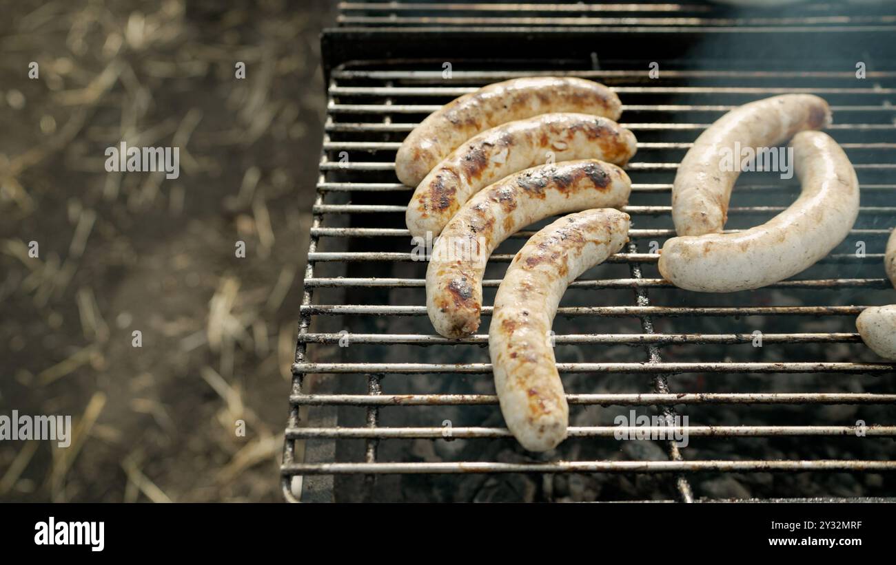 Le salsicce vengono fritte su un barbecue. Bratwurst o Hot Dogs on Grill with Flames. Foto Stock