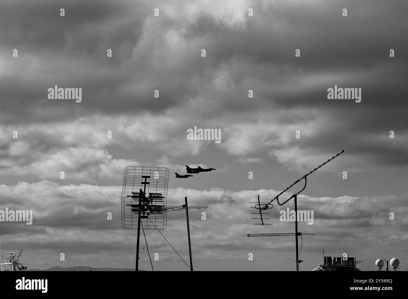 Nuvole scure si riuniscono mentre i getti dei combattenti tagliano il cielo sopra le vecchie antenne sul tetto Foto Stock