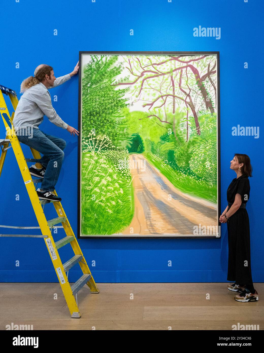 Londra, Regno Unito. 12 settembre 2024. Un tecnico e un membro dello staff con "l'arrivo della primavera a Woldgate, East Yorkshire nel 2011 (ventiundici) - 16 maggio" di David Hockney (stima £ 280.000 - 400,0000 in anteprima dei lavori in vendita di David Hockney a Phillips in Berkeley Square. I lotti saranno messi all'asta il 19 settembre. Crediti: Stephen Chung / Alamy Live News Foto Stock