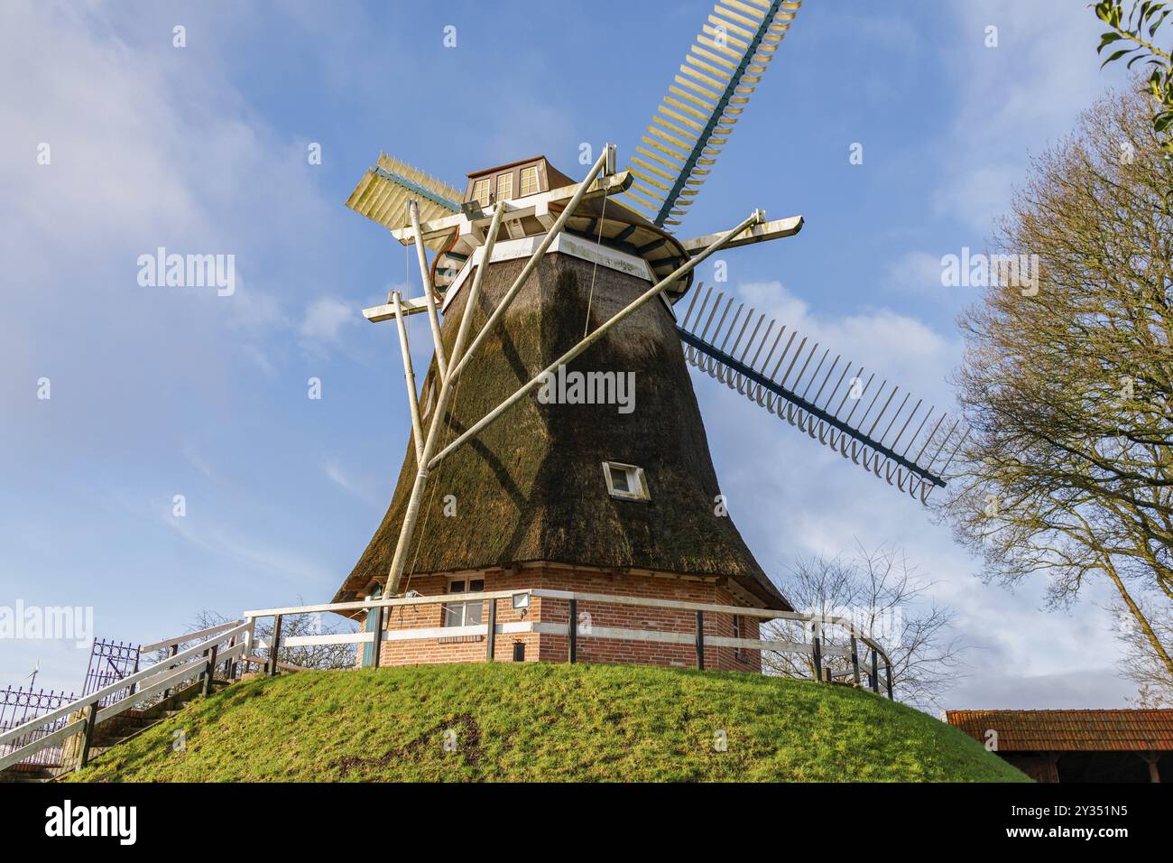 Mulino a vento su una collina verde, circondato da alberi e sotto un cielo blu, burlage, frisia orientale, germania Foto Stock