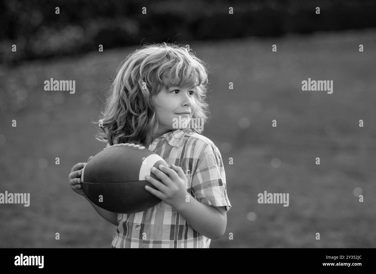 Ritratto di bambino con palla da rugby. Football americano. Bambino pronto a lanciare un calcio. Concetto di sport per bambini. Attività sportive per bambini all'aperto. Foto Stock