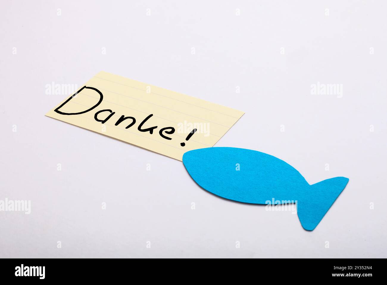 Danke! Parola tedesca scritta a mano su carta beige. Pesce blu nell'angolo. Isolato su bianco. Spazio libero per il testo. Foto Stock
