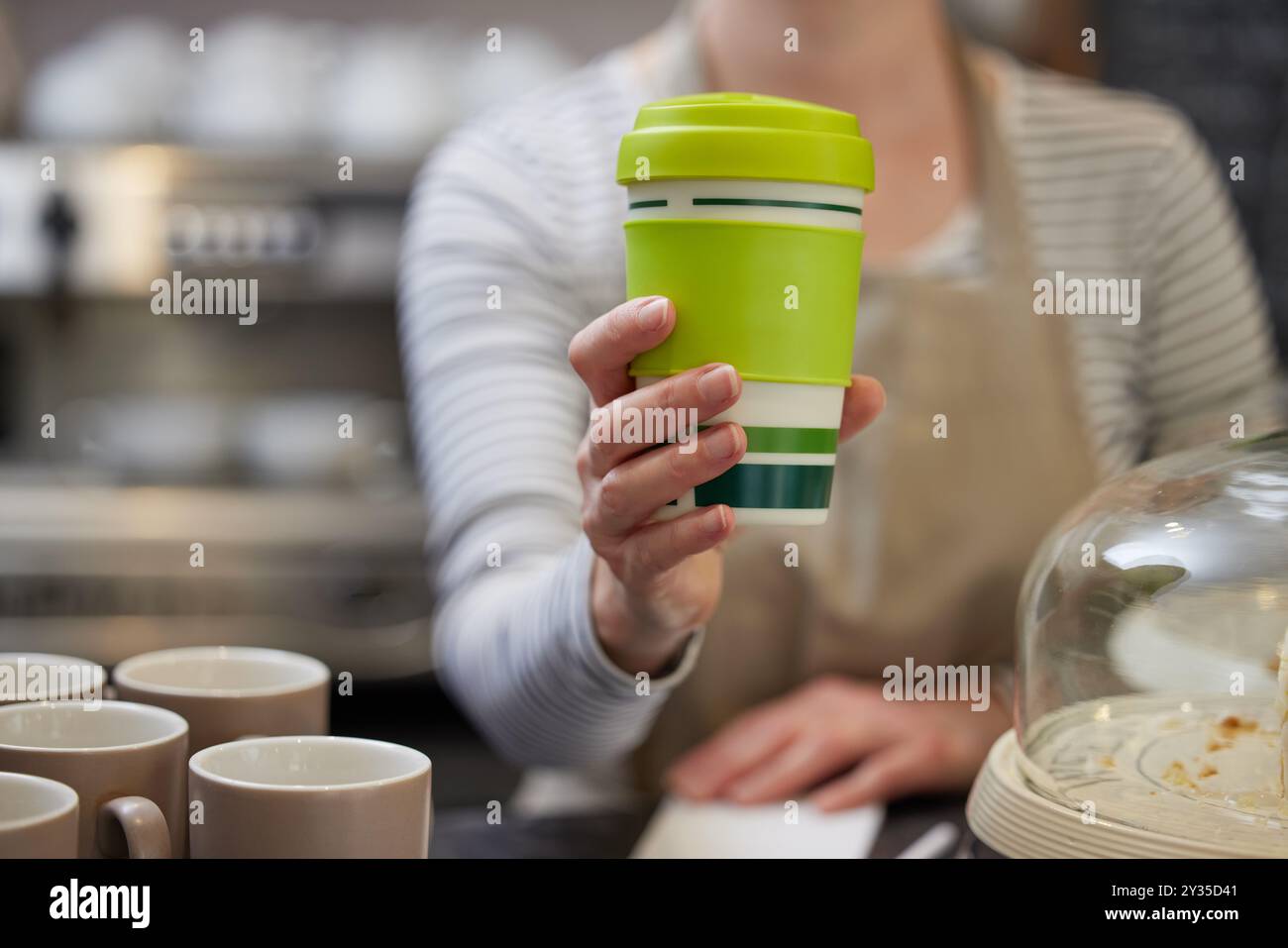 Primo piano di una lavoratrice al caffè che serve caffè o bevande calde in una tazza riutilizzabile sostenibile Foto Stock