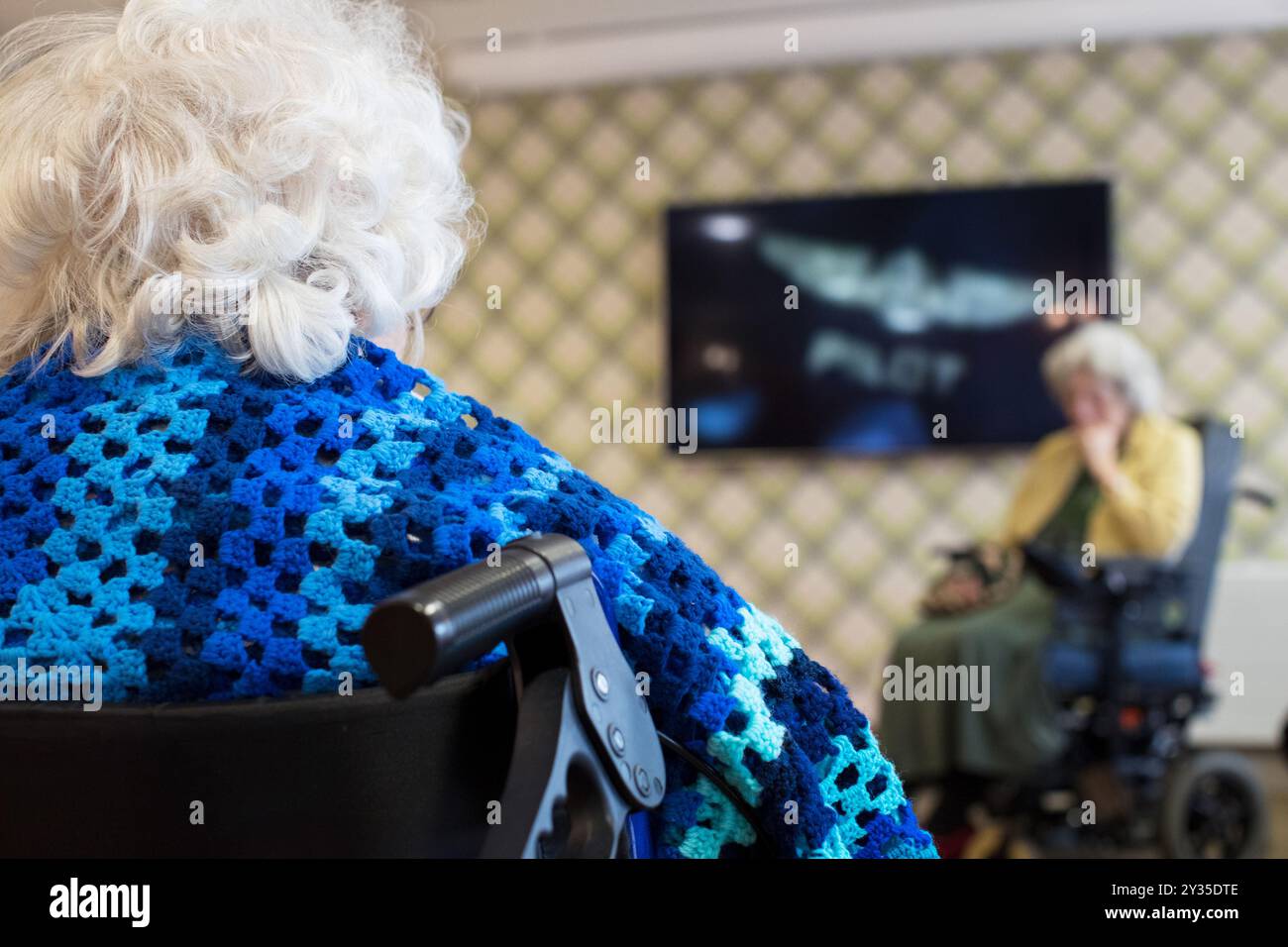 Anziani non identificabili in casa di cura seduti su sedie a rotelle nella sala dei residenti a guardare la TV Foto Stock