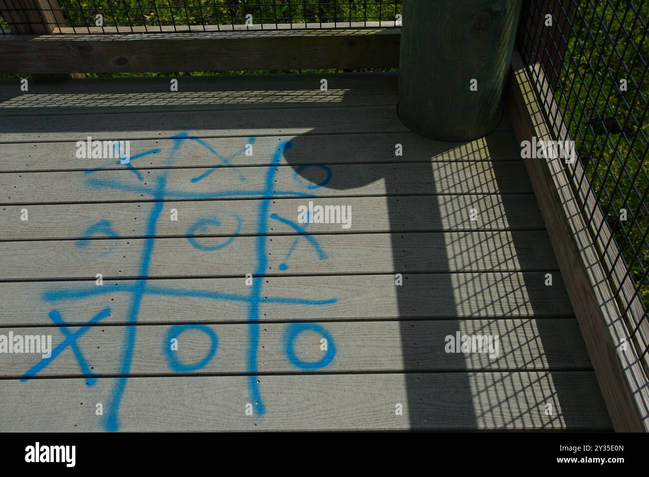 Ammira il TIC-tac-toe blu verniciato a spruzzo sulla passerella di legno su una piattaforma della torre. Luce solare e ombra che fuoriescono dalla rete metallica Foto Stock