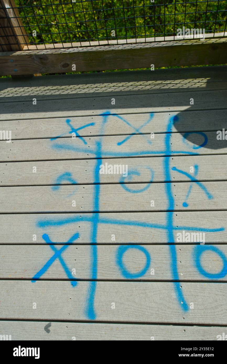 Ammira il TIC-tac-toe blu verniciato a spruzzo sulla passerella di legno su una piattaforma della torre. Luce solare e ombra che fuoriescono dalla rete metallica Foto Stock