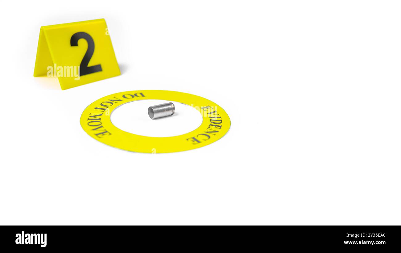 Involucro di un proiettile esaurito collocato all'interno di un cerchio giallo, etichettato con il testo "Evidence, do not move" (prova, non spostare), con un'etichetta sfocata con il numero 2, posta contro una b bianca Foto Stock