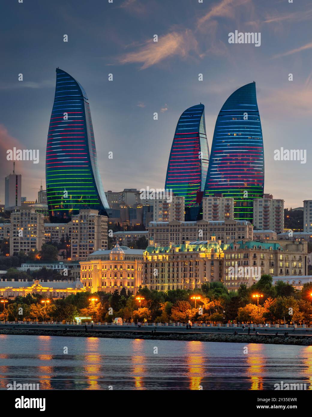 Le Torri della fiamma si ergono alte contro il cielo serale, illuminate dalla colorata bandiera dell'Azerbaigian e riflettono sull'acqua. Il vivace display mette in risalto le moderne realizzazioni architettoniche di Baku Foto Stock