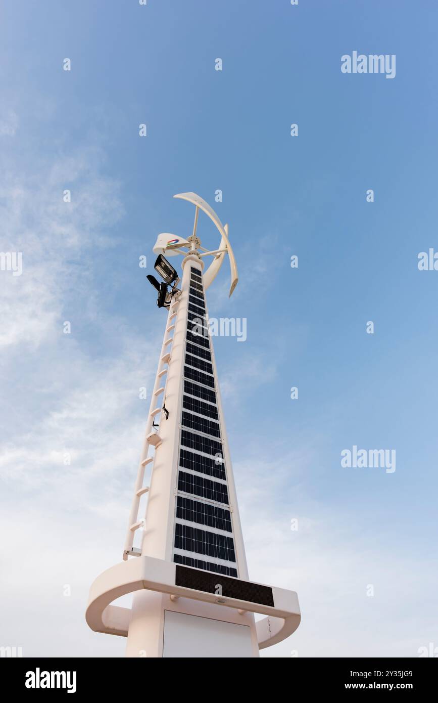 Vista verticale di un sistema ibrido di turbine solari ed eoliche in Medio Oriente, contro un cielo azzurro brillante, tecnologia avanzata per le energie rinnovabili Foto Stock
