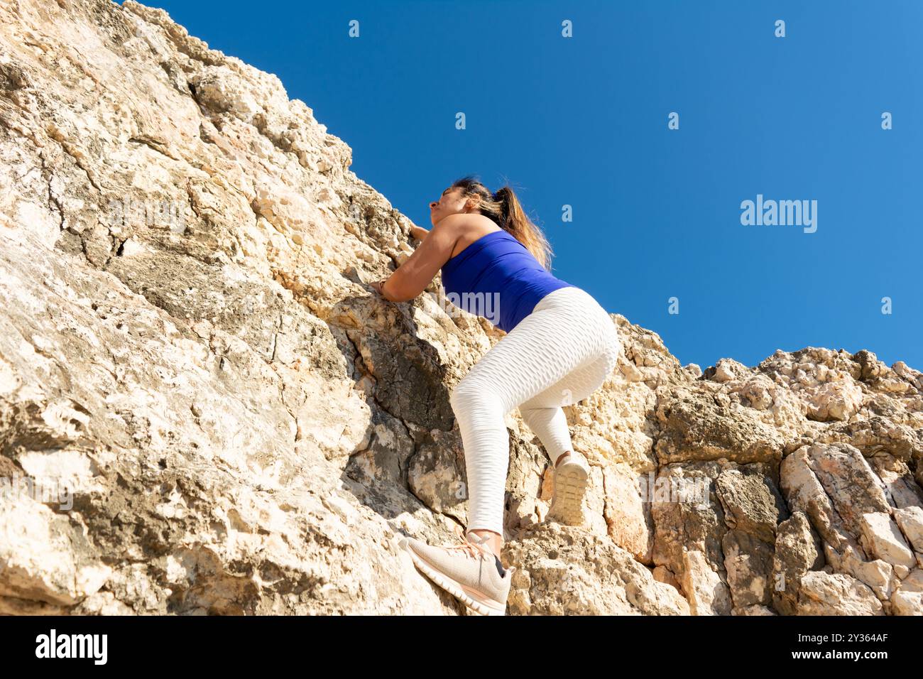 Donna che arrampica su un terreno roccioso all'aperto sotto un cielo azzurro, mostrando atletismo e determinazione, donna latina, mezza età, all'aperto, arrampicata Foto Stock