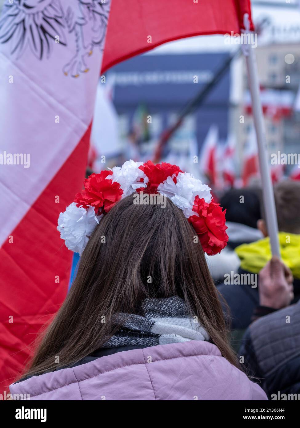 Primo piano sulla testa di una ragazza con corona di fiori bianchi e rossi durante la manifestazione patriottica. Varsavia, Polonia. Sfondo sfocato. Foto Stock