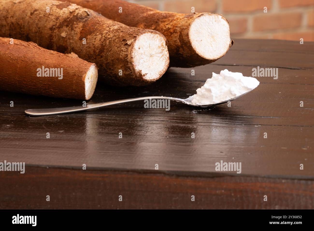 Tre radici di manioca su un tavolo di legno con un cucchiaio pieno di farina di tapioca davanti a loro. Foto Stock