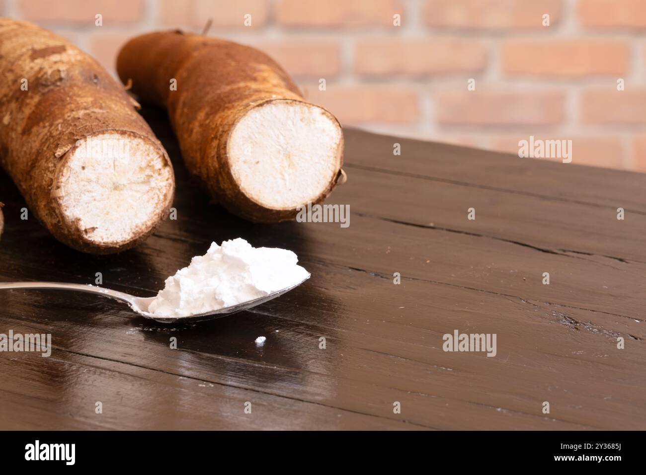 Un cucchiaio con farina di tapioca in primo piano e radici di manioca sullo sfondo. Foto Stock