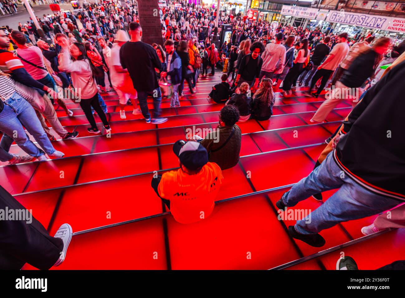 Splendida vista della affollata scalinata rossa di Times Square, New York, con persone che camminano e sedute, catturando la vibrante energia della città di notte. Nuovo Foto Stock