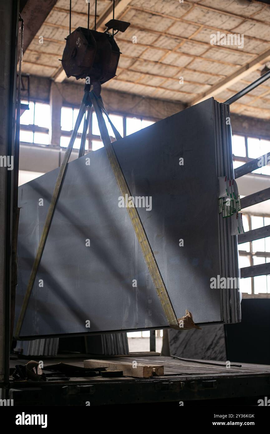 Gru industriale che solleva una lastra di marmo all'interno di una fabbrica, evidenziando materiali naturali e processi meccanici Foto Stock