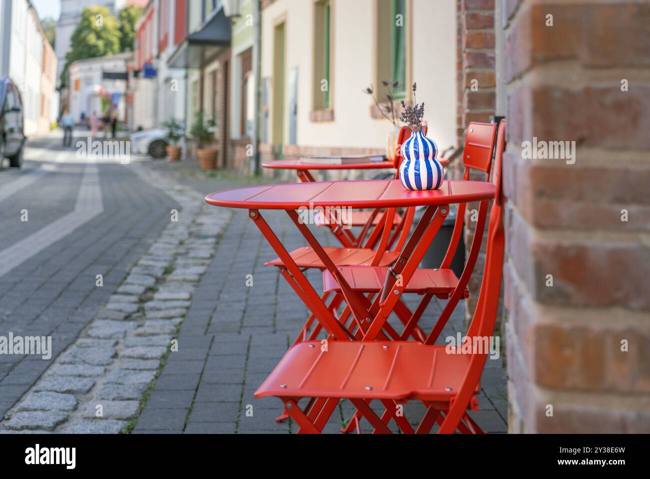 Tavolo all'aperto del ristorante con giardino. Strada cittadina. Pianta blu sedia rossa Foto Stock