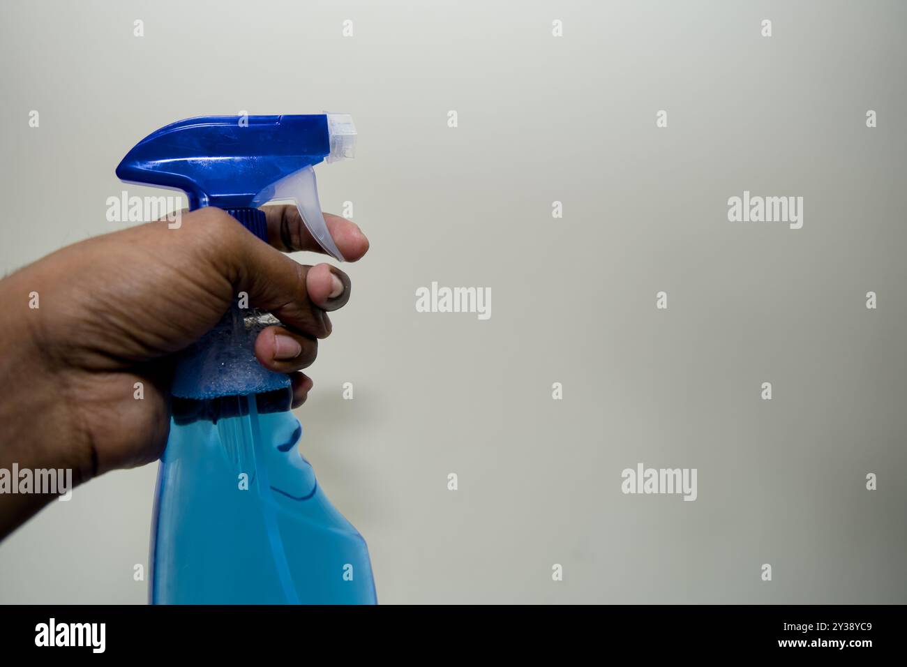 Pronti a pulire! Primo piano di una mano che regge una bomboletta spray blu su uno sfondo neutro. Foto Stock