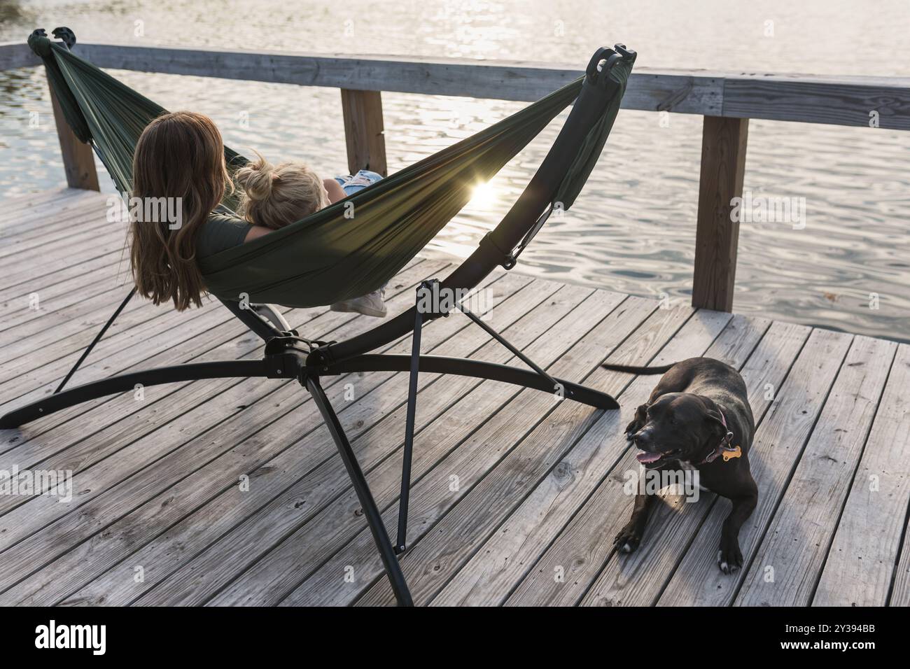 Persone che si rilassano nell'amaca sul lago con cani nelle vicinanze Foto Stock