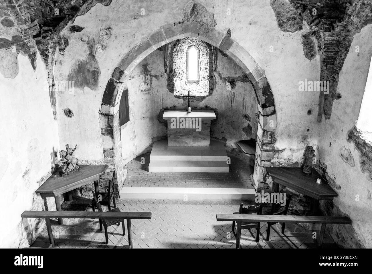 Una vista serena della cappella medievale all'interno del Castello di Aggstein, che mette in risalto l'altare, la finestra ad arco e le panchine in legno rustiche sotto la luce naturale soffusa. Wachau, Austria. Foto in bianco e nero Foto Stock